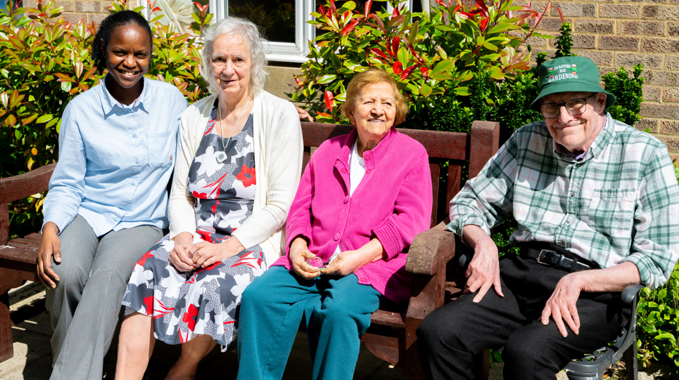 Three residents and a colleague sat on a garden bench on a sunny day