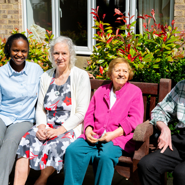 Three residents and a colleague sat on a garden bench on a sunny day
