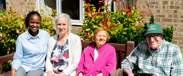 Three residents and a colleague sat on a garden bench on a sunny day