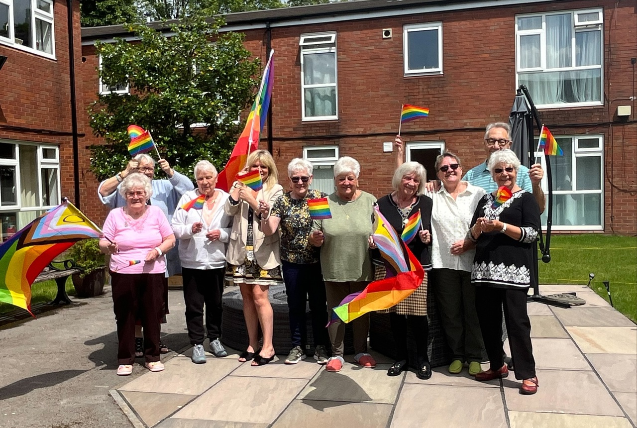 A group of residents standing in a group with colleagues smiling, waving Pride flags