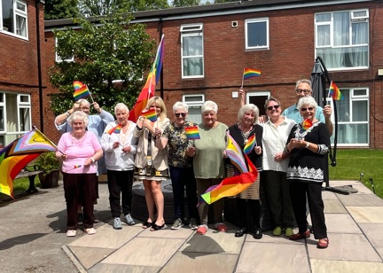 A group of residents standing in a group with colleagues smiling, waving Pride flags