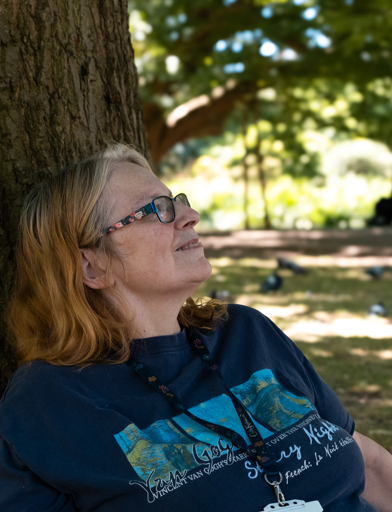 A resident sitting under a tree on grass in a local park 