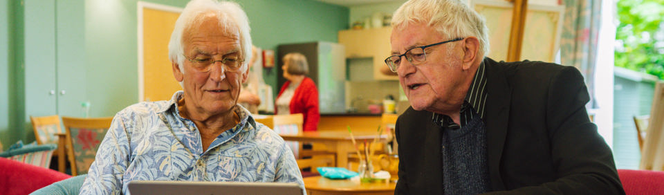 Two caucasian men sitting at a table looking at a computer tablet 