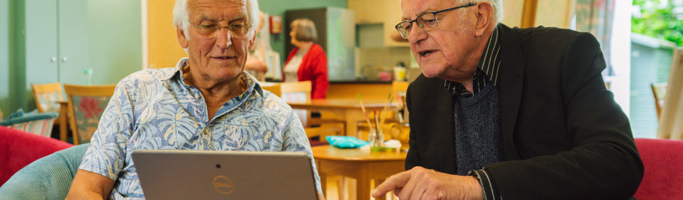 Two caucasian men sitting at a table looking at a computer tablet 