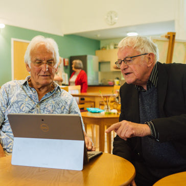 Two caucasian men sitting at a table looking at a computer tablet