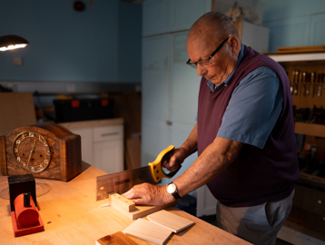 A resident sawing a piece of wood in the woodwork room