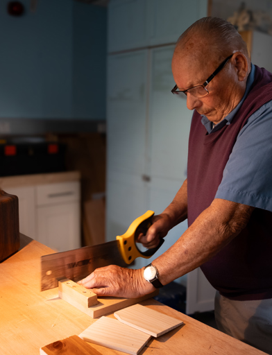 A resident sawing a piece of wood in the woodwork room 