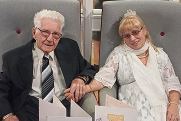 A couple sit and hold hands surrounded by cards and flowers