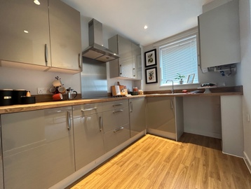 A kitchen inside an apartment at Askern Vale featuring grey cupboards and a light brown wood worktop with pictures of fruit on the wall