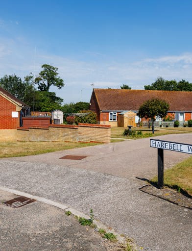 Entrance driveway to the scheme with bungalows, landscaped communal gardens and welcome signs. 