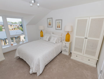 A bedroom inside an apartment at Bowland View. Featuring a bed with cream bedsheets, a cream wardrobe and two bedside tables with lamps