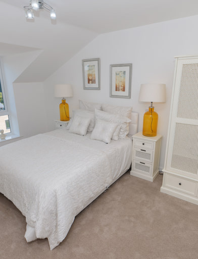 A bedroom inside an apartment at Bowland View. Featuring a bed with cream bedsheets, a cream wardrobe and two bedside tables with lamps