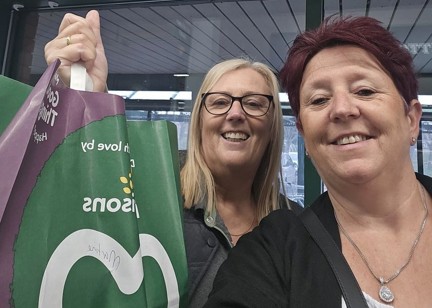 A Housing 21 employee and a Morrisons employee smiling and holding up a Morrisons bag full of shopping.