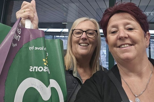A Housing 21 employee and a Morrisons employee smiling and holding up a Morrisons bag full of shopping.