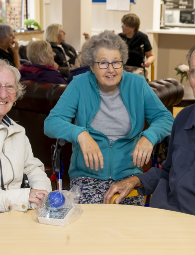 Three residents sit around a table and smile for the camera 