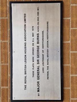 A wall plaque which reads: "The Royal British Legion Housing Association Limited. These flats were opened on 9th May 1976 by Major General Sir George Burns, KCVO, CB, SDO, OBE, MC. Lord Lieutenant of Hertfordshire, Patron, the Royal British Legion, Hertfordshire."