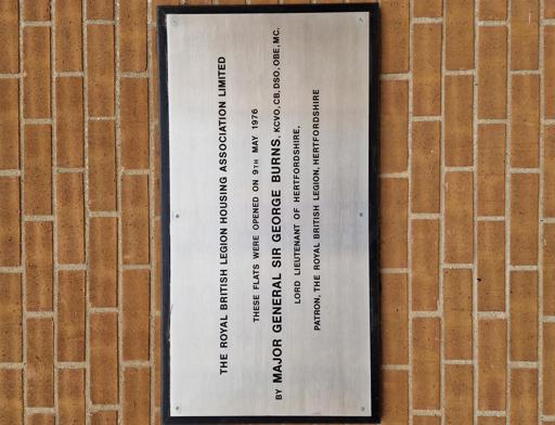 A wall plaque which reads: "The Royal British Legion Housing Association Limited. These flats were opened on 9th May 1976 by Major General Sir George Burns, KCVO, CB, SDO, OBE, MC. Lord Lieutenant of Hertfordshire, Patron, the Royal British Legion, Hertfordshire." 