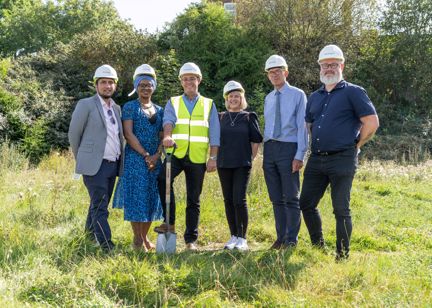 Housing 21 employees standing outside on grass wearing hard hats and holding a spade. 