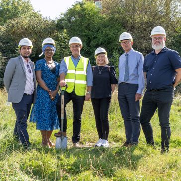 Housing 21 employees standing outside on grass wearing hard hats and holding a spade. 