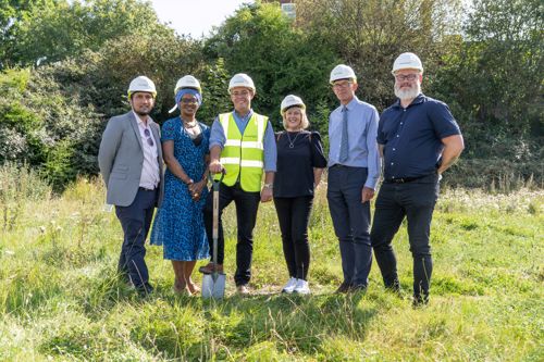 Housing 21 employees standing outside on grass wearing hard hats and holding a spade.