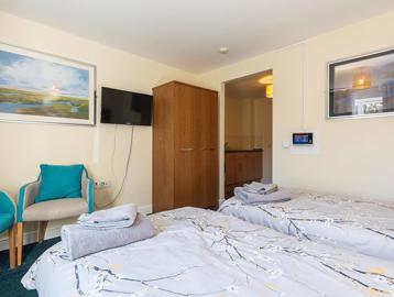Two single beds, two chairs and a wall mounted TV in the bedroom of an apartment