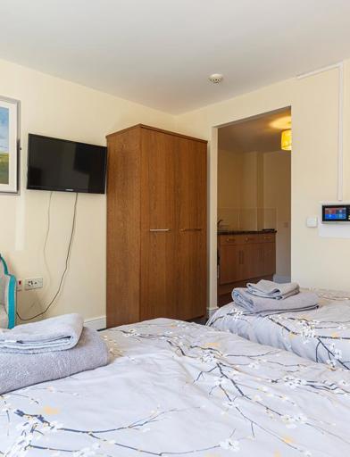 Two single beds, two chairs and a wall mounted TV in the bedroom of an apartment 