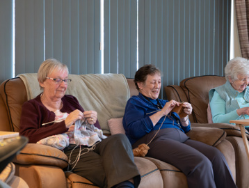 A group of three female residents sitting on a sofa whilst concentrating on knitting