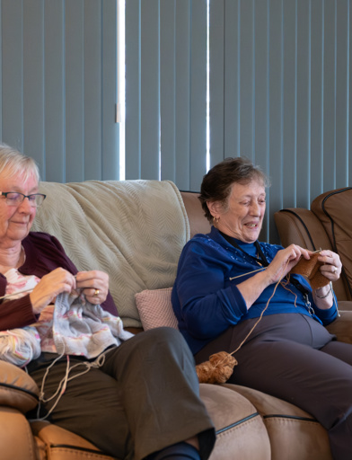 A group of three female residents sitting on a sofa whilst concentrating on knitting 