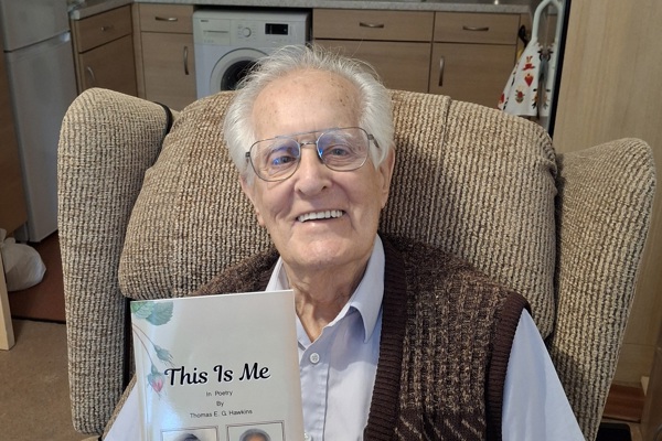 Elderly gentleman in knitted waistcoat, holding up his new poetry book 'this is me'