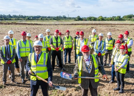Employees of Housing 21 along with special guests wearing high-vis jackets and hard hats whilst holding spades standing outside.