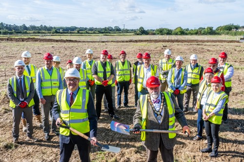 Employees of Housing 21 along with special guests wearing high-vis jackets and hard hats whilst holding spades standing outside.