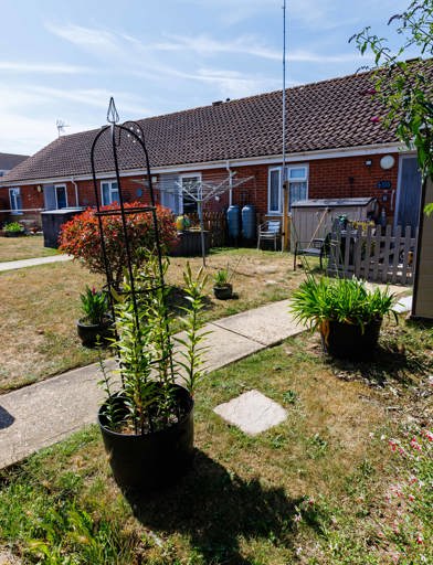Front of the property with gardens featuring hedges, potted plants and solar-powered lights. 