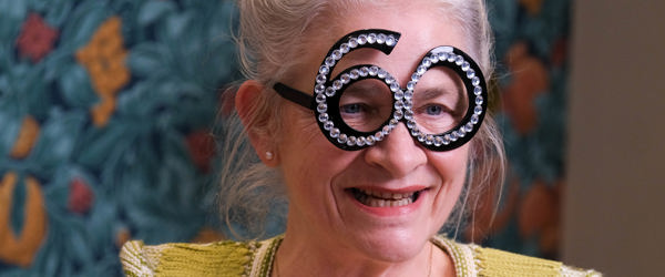 Resident wearing party glasses in the shape of the number 60 and holding a wine glass