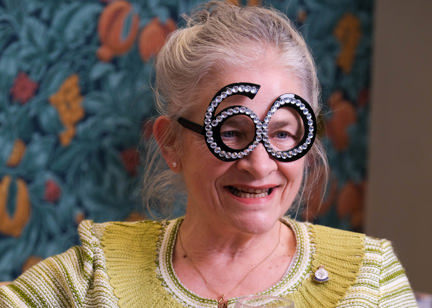 Resident wearing party glasses in the shape of the number 60 and holding a wine glass