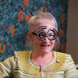 Resident wearing party glasses in the shape of the number 60 and holding a wine glass