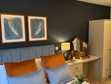 A double bedroom with blue walls featuring a dressing table and wardrobe with a double bed with blue and white sheets.