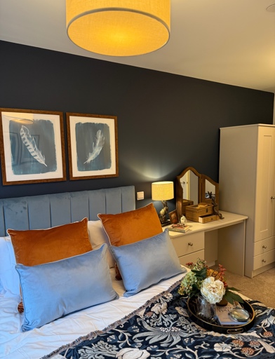 A double bedroom with blue walls featuring a dressing table and wardrobe with a double bed with blue and white sheets. 
