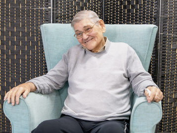 A resident sitting in an arm chair smiles at the camera