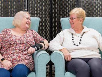 Two residents sitting in armchairs smiling at each other