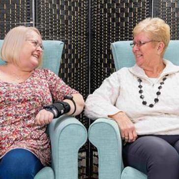 Two residents sitting on arm chairs smiling