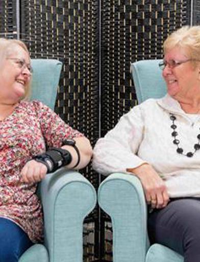 Two residents sitting in armchairs smiling at each other 