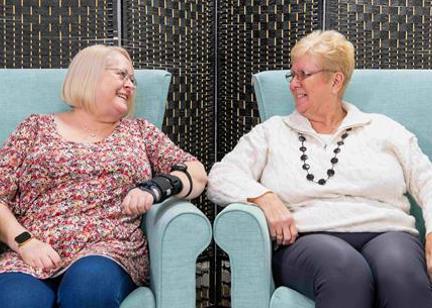 Two residents sitting on arm chairs smiling