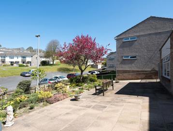 A hard-landscaped communal patio garden at the front of the scheme with plans, ornaments and bench