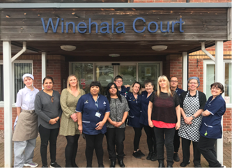 Housing 21 care workers standing outside the front door to Winehala Court.