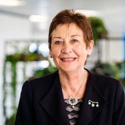 A lady dressed in formal office attire faces into the camera and smiles 