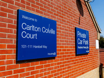 Exterior signage on a red brick wall with a blue sign welcoming visitors to Carlton Colville Court.