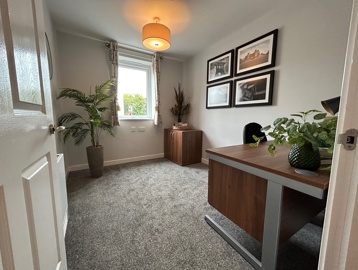 A spare bedroom inside an apartment at Askern Vale featuring a desk with a small plant and a large plant in the room on the carpet