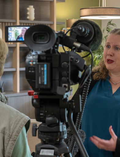 Lady dressed in a smart blazer, being interviewed while stood talking to a camera 