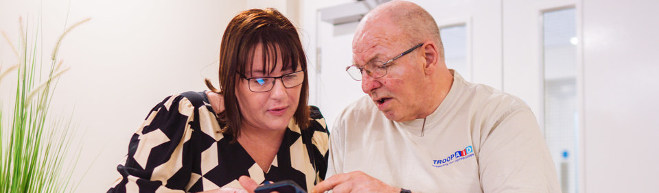 A female employee helps a male Retirement Living resident to find something on their mobile phone 