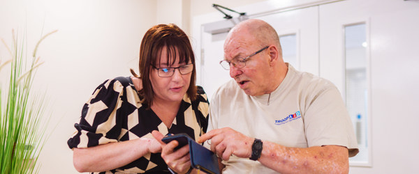 An employee helping a Retirement Living resident to find something on their mobile phone